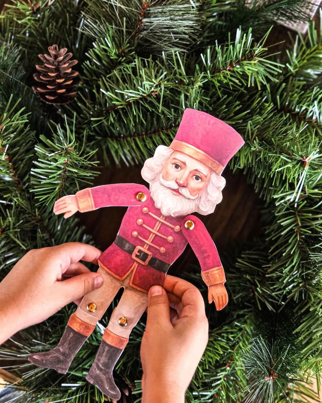 Hand holding a paper toy figure of a character from Nutcracker Book Study in front of a Christmas tree